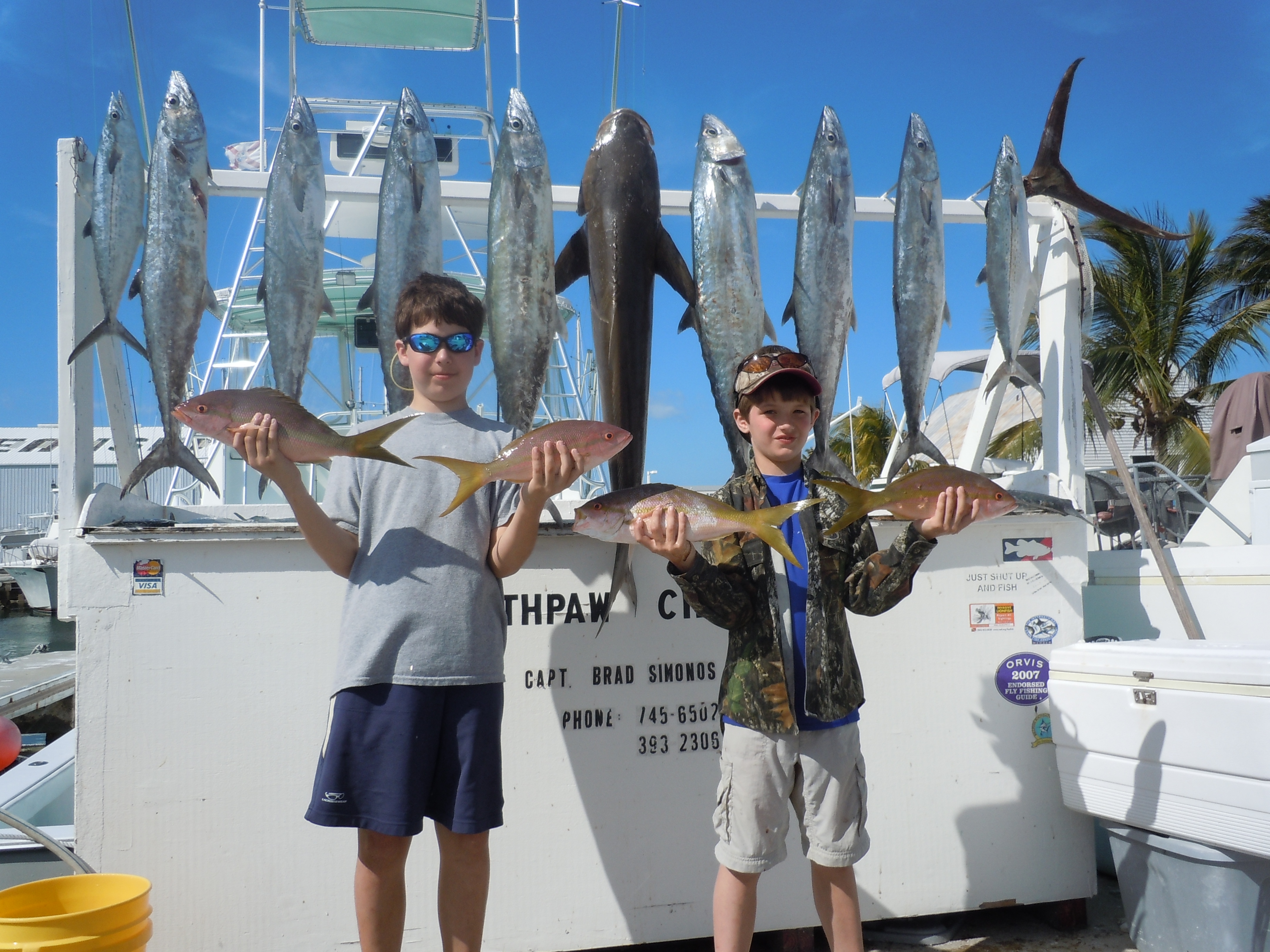 2 kids holding 4 yellowtail snappers and kingfish hanging on the rack